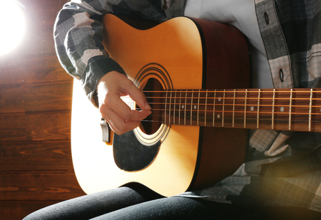 Guitarist plays guitar on wooden background, close up