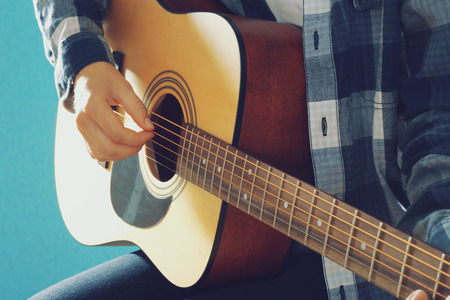 Musician plays guitar on blue background, close up