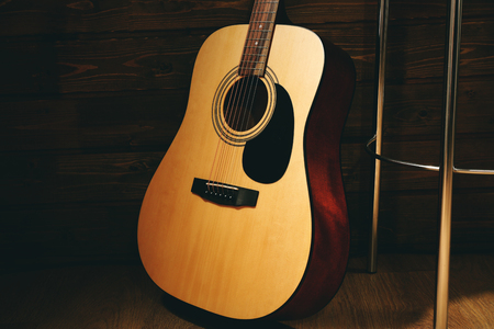 Acoustic guitar propped on wooden wall with bar stool in the roomの写真素材