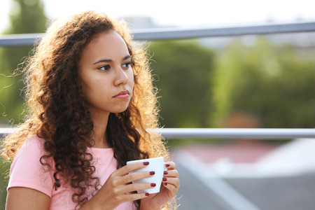 Pretty young woman in pink dress drinking coffee at summer terraceの写真素材