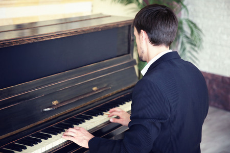 Handsome man in black suit plays piano in the classの写真素材