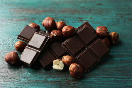 Black chocolate pieces with nuts on color wooden background
