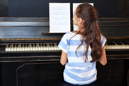 Cute little musician girl plays piano, back viewの写真素材