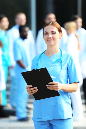 Portrait of woman doctor with clipboard in hands standing against unfocused group of medicsの写真素材