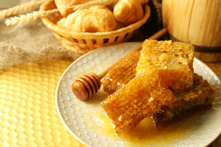 Honeycombs on plate, hot buns in basket on wooden background
