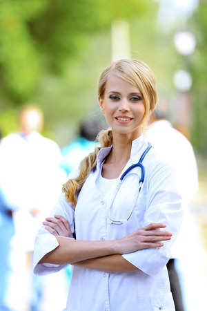 Beautiful smart woman doctor with clipboard in hands standing against blurred group of medicsの写真素材