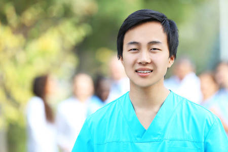 Young smiling doctor standing against unfocused group of medical workers