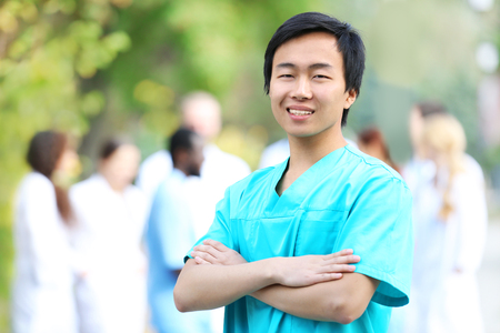 Young smiling doctor standing against unfocused group of medical workersの写真素材