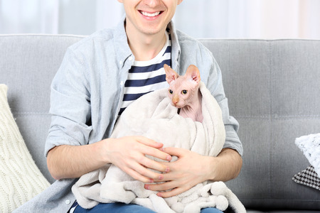 Young man sitting with cat on couch at homeの写真素材