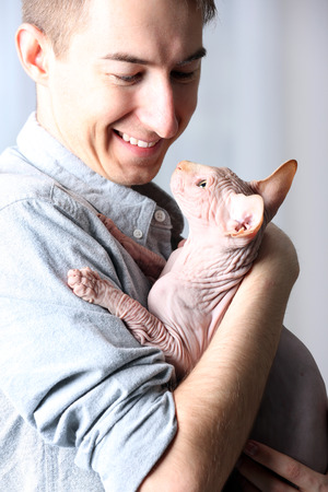 Young handsome man holding a cat on light tulle backgroundの写真素材