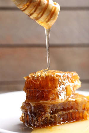 Honey dripping on honeycombs on plate on wooden background
