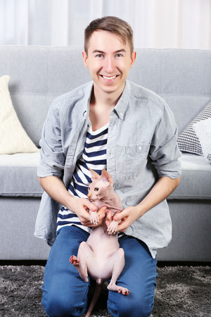Young handsome man sitting with cat on floor at homeの写真素材