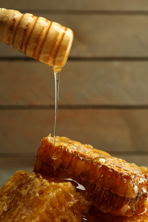 Honey dripping on honeycombs, on wooden backgroundの写真素材