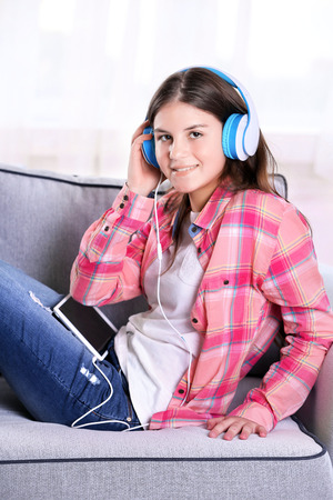 Young pretty girl listening to music on the sofa in her roomの写真素材