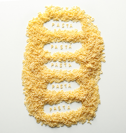 Composition with raw alphabet pasta on white background 