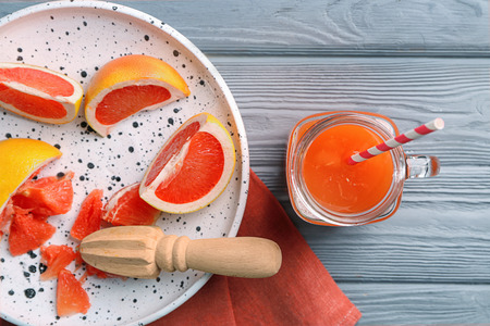 Mason jar of fresh citrus juice and plate with grapefruit on tableの写真素材