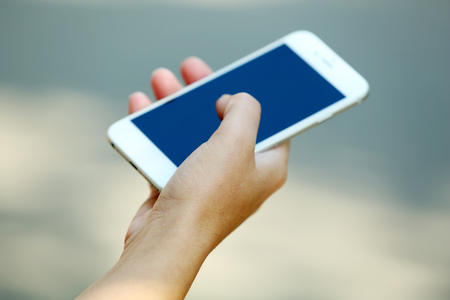 A female hand holding a mobile phone outdoors, on blurred backgroundの写真素材