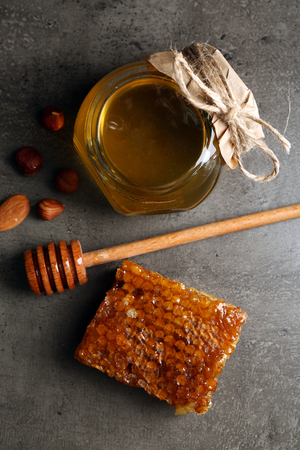Honeycomb, glass pot with honey and nuts on gray backgroundの写真素材