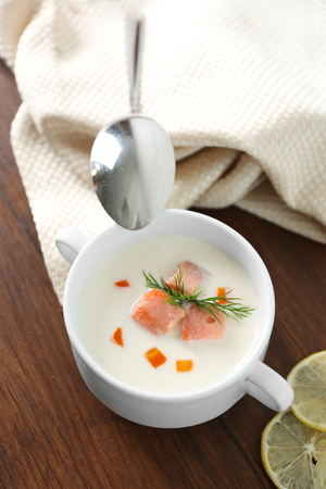 Delicious salmon cream soup with spoon on wooden table, which served with sliced lemon and spicesの写真素材
