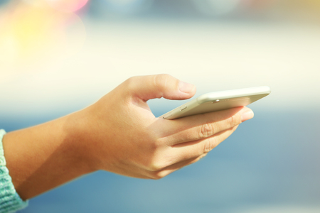 A female hand holding a mobile phone outdoors, on blurred backgroundの写真素材