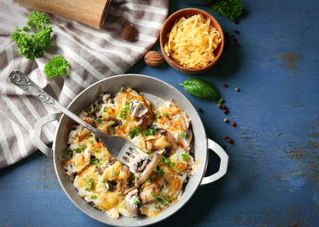 Roasted mushrooms, chicken and cheese gratin in pan, on color wooden backgroundの写真素材