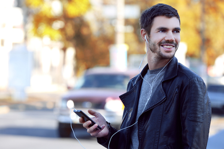 Young man listening to music and walking along the streetの写真素材