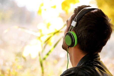 Young man sitting under the tree and listening to musicの写真素材