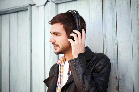 Young man listening to music on a house wall backgroundの写真素材