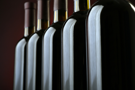 Wine bottles in a row on dark red background, close upの写真素材