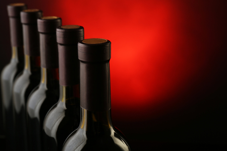 Wine bottles in a row on dark red background, close up