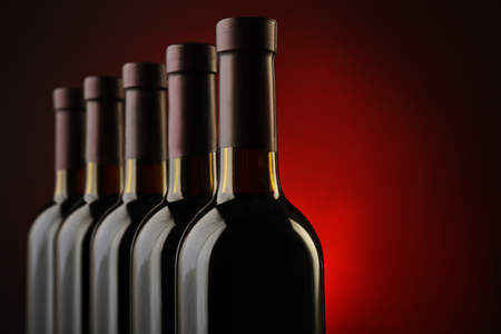 Wine bottles in a row on dark red background, close upの写真素材
