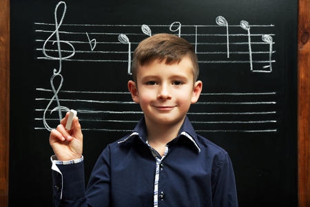 Cute boy standing at the blackboard with musical notes, in the classroomの写真素材