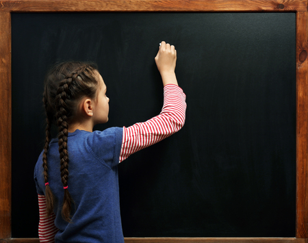 Cute girl posing at the clean blackboard, in the classroomの写真素材