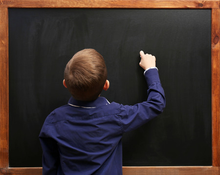 Back view of a boy posing at the blackboard, in the classroom