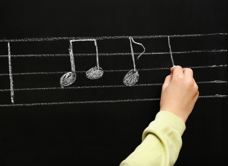 View on boy's hand writing at the blackboard with musical notes, close-upの写真素材