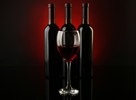 Wine glass against bottles in a row on dark red background, close upの写真素材