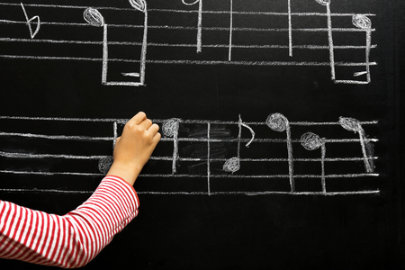 View on girl's hand writing at the blackboard with musical notes, close-upの写真素材