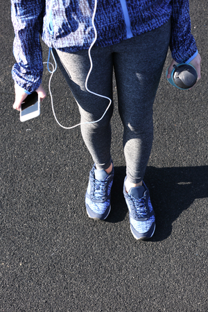 Woman in sports clothes and sneakers with cellphone and bottle