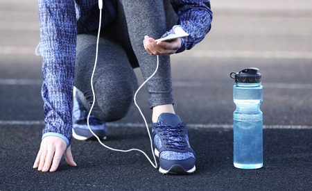 Woman in sports clothes and sneakers with cellphone and bottle