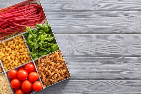 Boxes with different uncooked pasta and products on wooden background