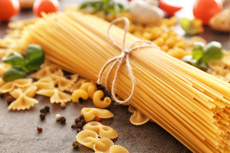 Tied spaghetti and other uncooked pasta on tableの写真素材