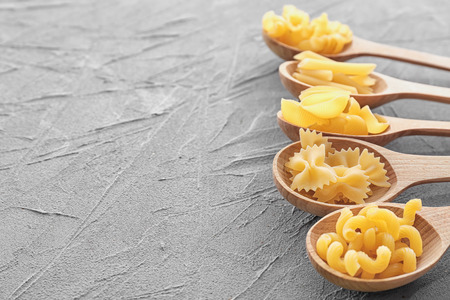 Wooden spoons with different uncooked pasta on grey tableの写真素材