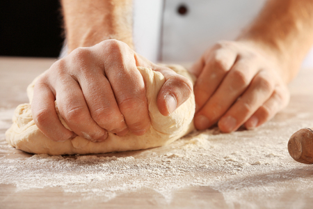 Hands kneading dough for pizza on the wooden table, close-upの写真素材