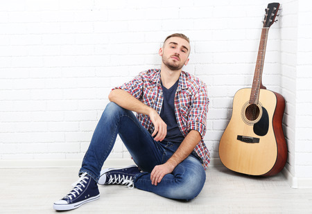 Young musician with guitar on light wall backgroundの写真素材