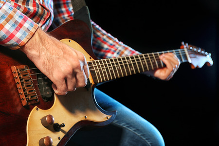 Young man playing on electric guitar close up