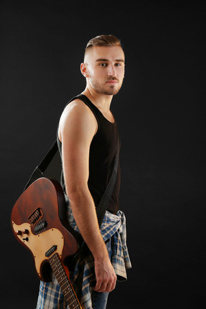 Young man with electric guitar on dark backgroundの写真素材