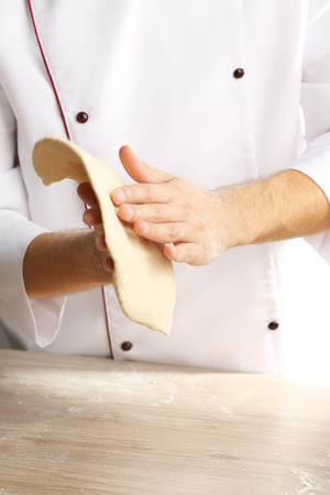 Hands preparing dough basis for pizza on the wooden table, close-upの写真素材