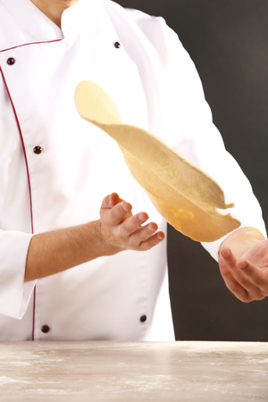 Man preparing dough basis for pizza on the wooden table, close-upの写真素材