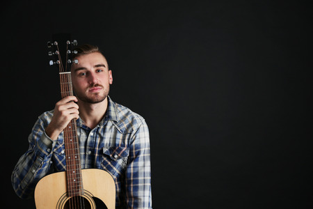 Young man with guitar on dark background