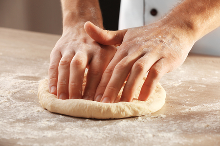 Hands kneading dough for pizza on the wooden table, close-upの写真素材